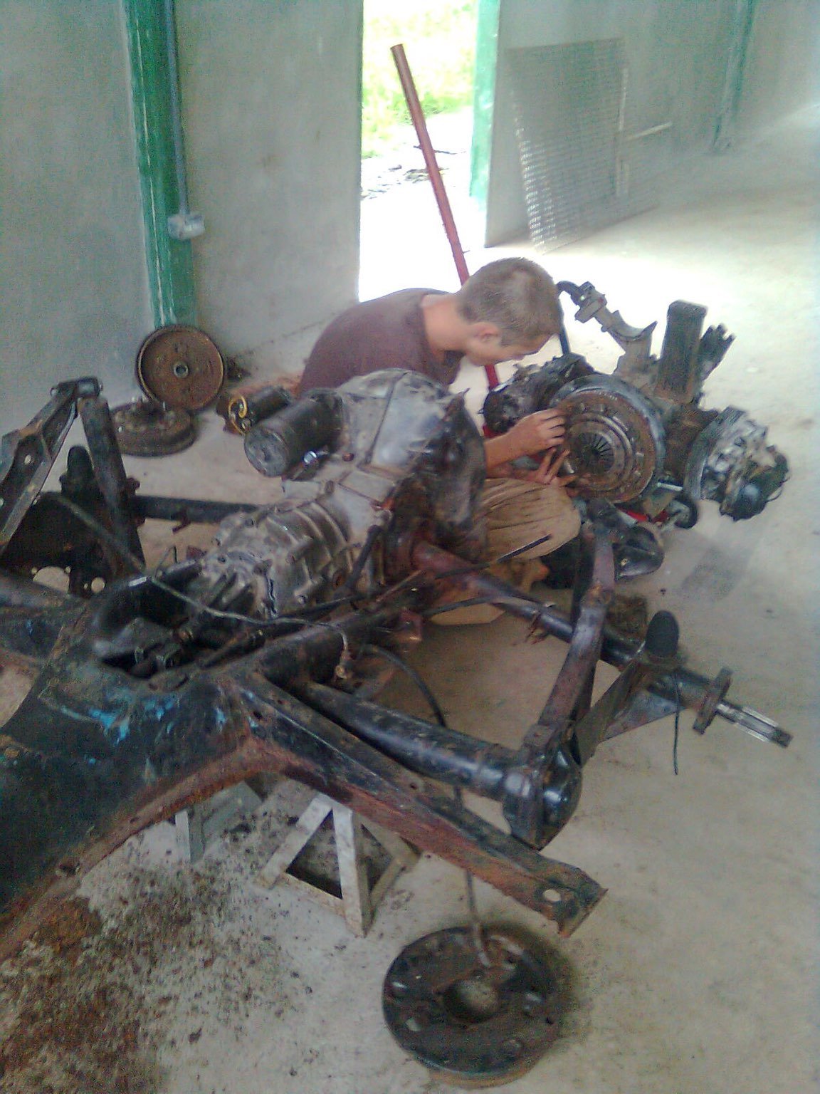 Mechanic shop with car parts everywhere. A person inspects the engine supported by a jack.