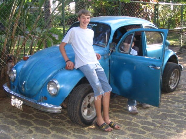 Some young boys crowd excitedly around a bright blue volkswagen beetle.